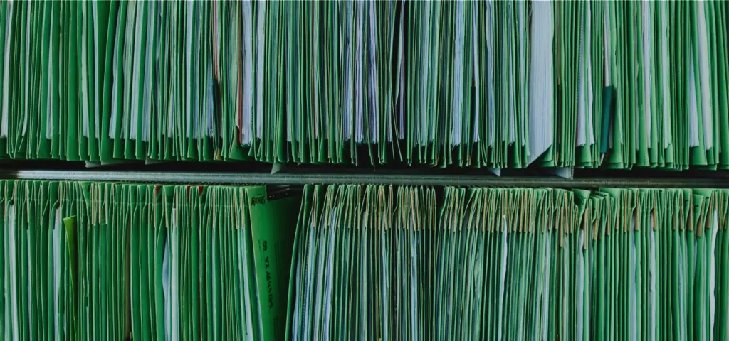 Nahaufnahme eines Regals voller grüner Aktenordner und Mappen, die dicht an dicht stehen. Die Unterlagen wirken sortiert und geordnet.