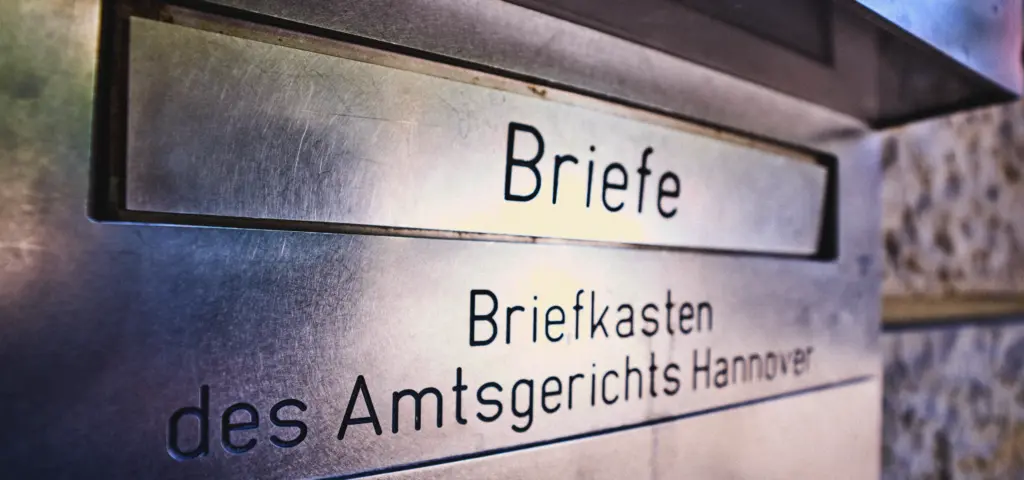 Nahaufnahme eines Briefkastens mit der Beschriftung „Briefe“ und „Briefkasten des Amtsgerichts Hannover“. Die Oberfläche besteht aus Metall und reflektiert das Licht.