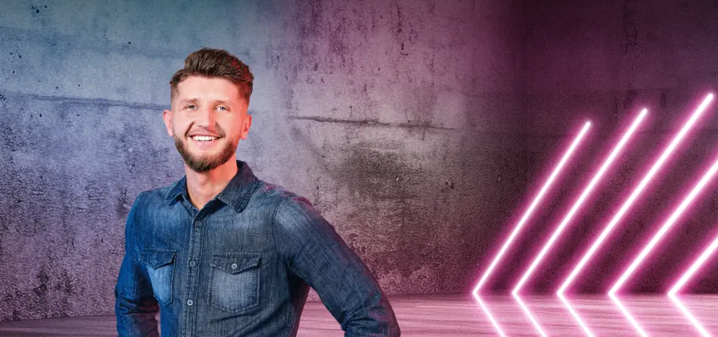 Eine Person steht lächelnd vor einer Betonwand mit blau-pinken Lichtverläufen. Rechts im Bild sind mehrere diagonale Neonlichtstreifen zu sehen, die in den Raum weisen. Die Szene wirkt modern und freundlich.