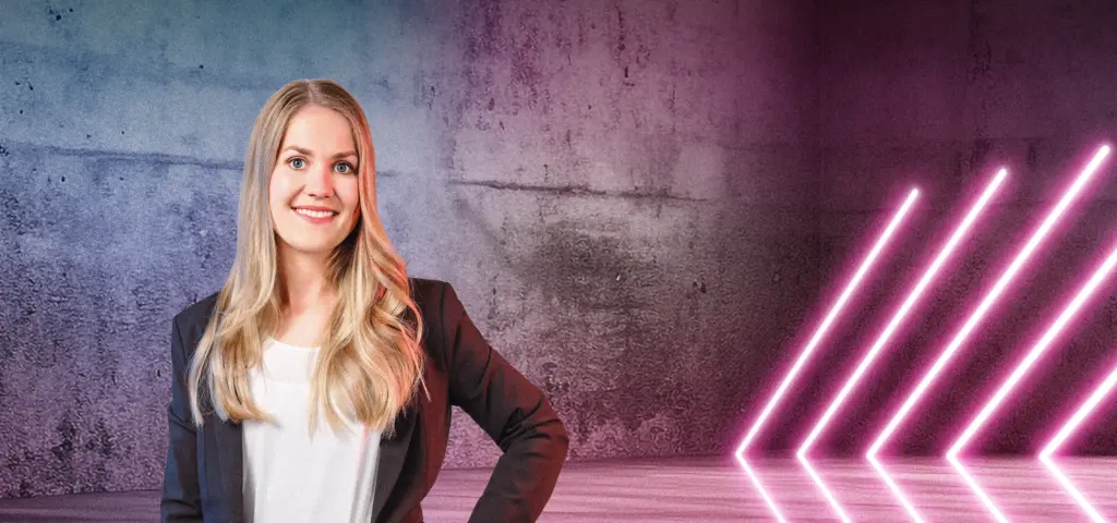 Eine Person steht lächelnd vor einer Betonwand mit blau-pinken Lichtverläufen. Rechts im Bild sind mehrere diagonale Neonlichtstreifen zu sehen, die in den Raum weisen. Die Szene wirkt modern und freundlich.