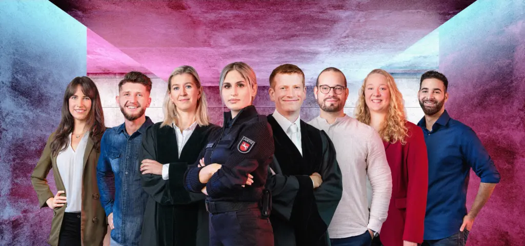 Acht Personen stehen nebeneinander vor einem farbigen Hintergrund mit blau-rosa Lichtverläufen. Sie blicken freundlich in die Kamera, einige mit verschränkten Armen. Die Gruppe vermittelt einen selbstbewussten und professionellen Eindruck. Die Person in der Mitte trägt eine blaue Uniform. Links und rechts von ihr stehen zwei Personen in Robe.