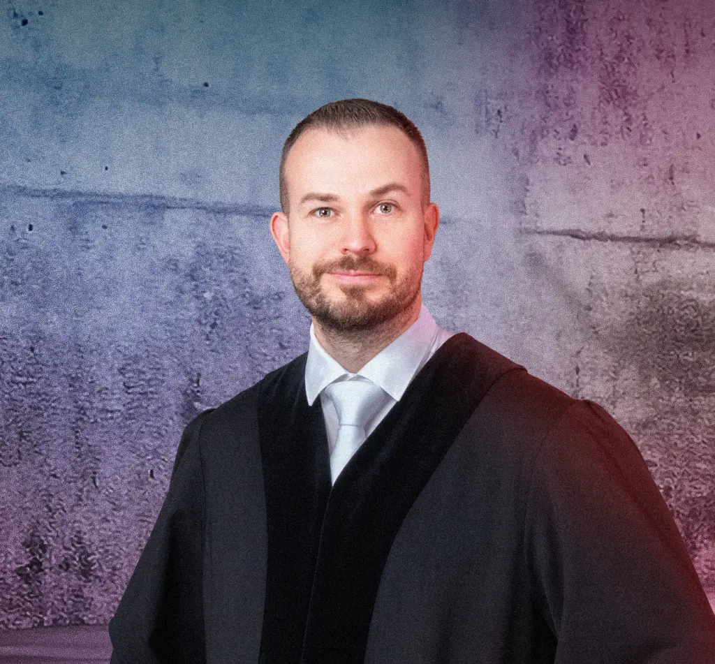 Eine Person in Robe steht lächelnd vor einer Betonwand mit blau-pinkem Lichtverlauf. Rechts im Bild leuchten mehrere diagonale Neonlichtstreifen. Die Szene wirkt modern und professionell.