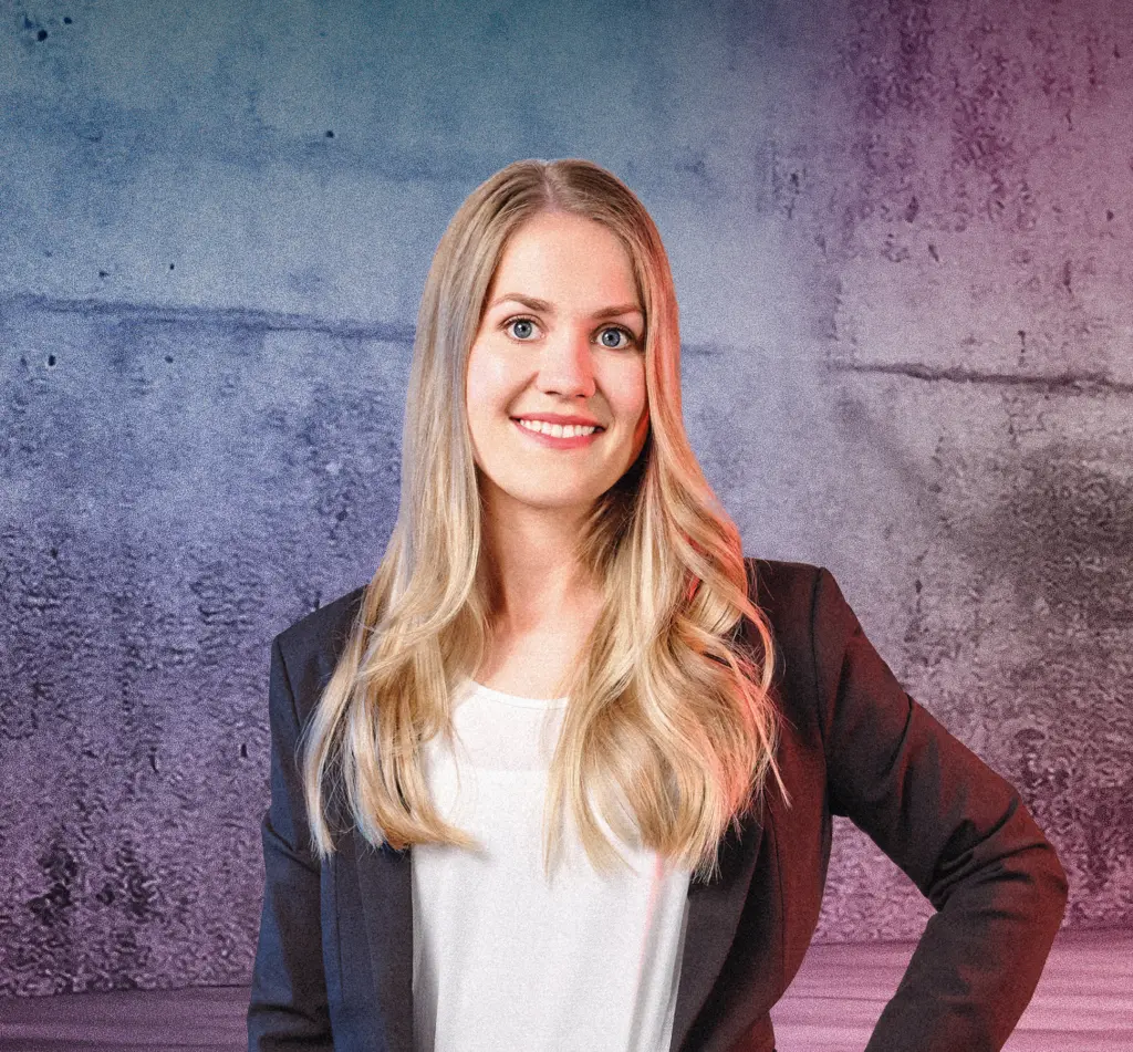 Eine Person steht lächelnd vor einer Betonwand mit blau-pinken Lichtverläufen. Rechts im Bild sind mehrere diagonale Neonlichtstreifen zu sehen, die in den Raum weisen. Die Szene wirkt modern und freundlich.